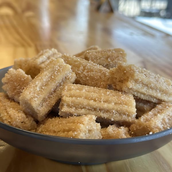 A bowl of golden-brown churro bites, coated in sugar and cinnamon, on a wooden table.