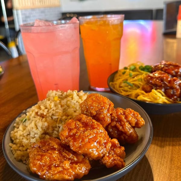 Itokos Grill's orange chicken with fried rice, noodles, and two colorful drinks on a wooden table.