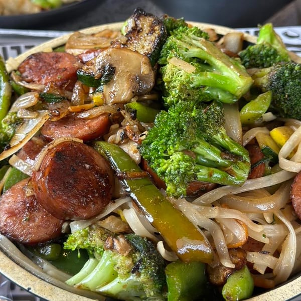 Close-up of a Japanese stir-fry with sliced sausage, broccoli, mushrooms, onions, and peppers.