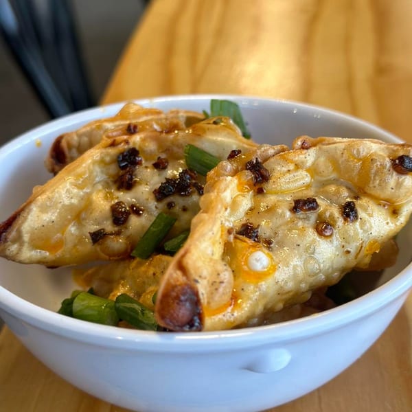 Close-up of Itokos Grill's Japanese gyoza, topped with chili oil and green onions in a white bowl.