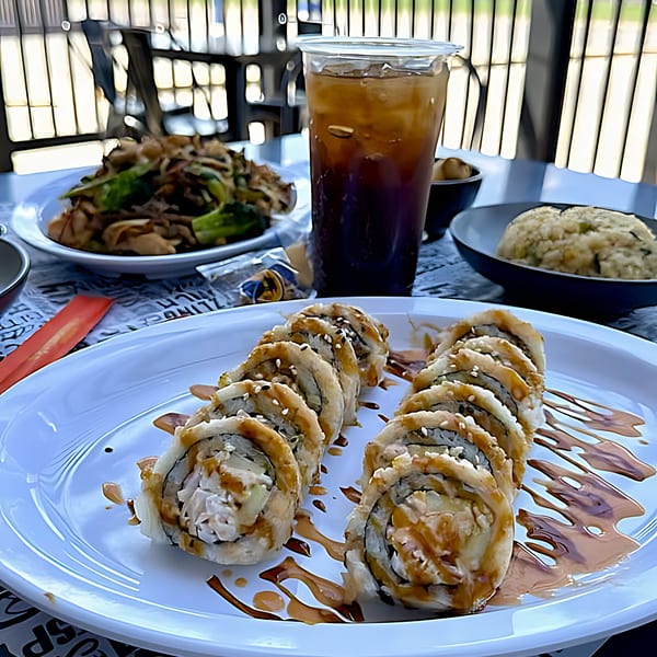 Itokos Grill's sushi rolls with sauce, fried rice, noodles, and iced tea on an outdoor table.