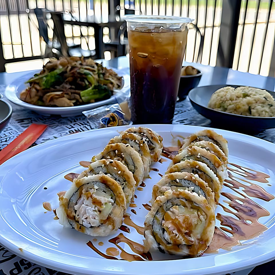 Itokos Grill's sushi rolls with sauce, fried rice, noodles, and iced tea on an outdoor table.